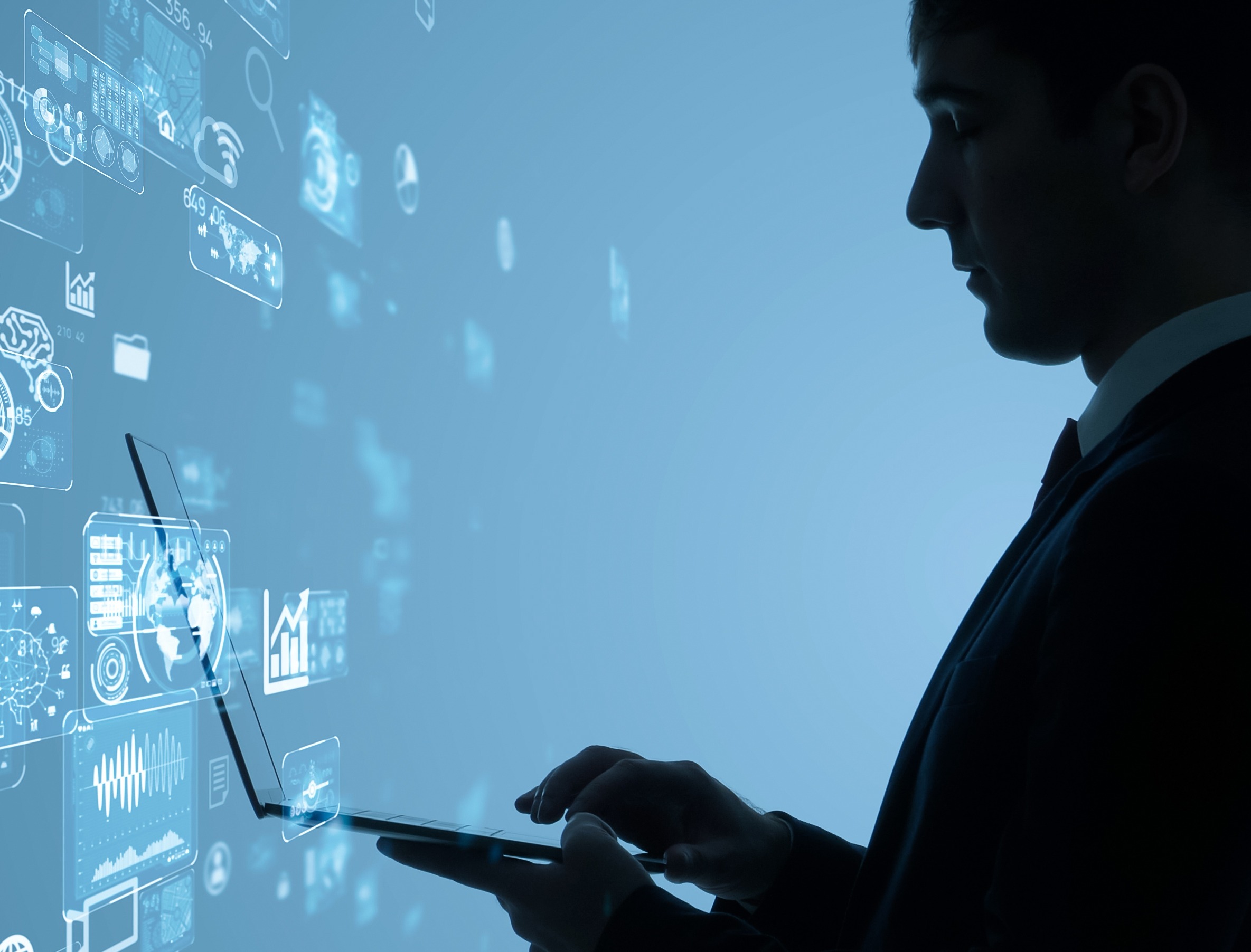 A businessman holds a laptop in front of a screen displaying data and icons.