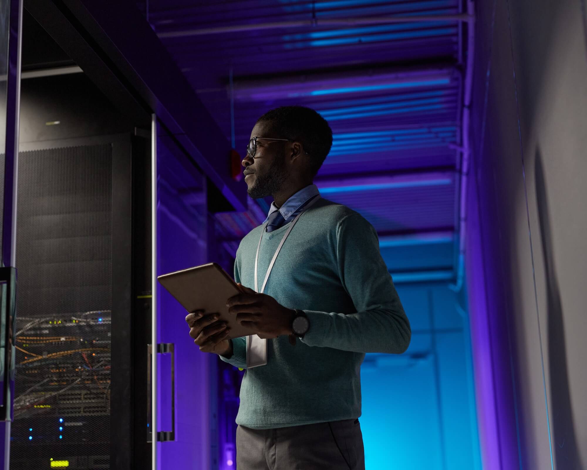 An employee holding a tablet stands in a server room