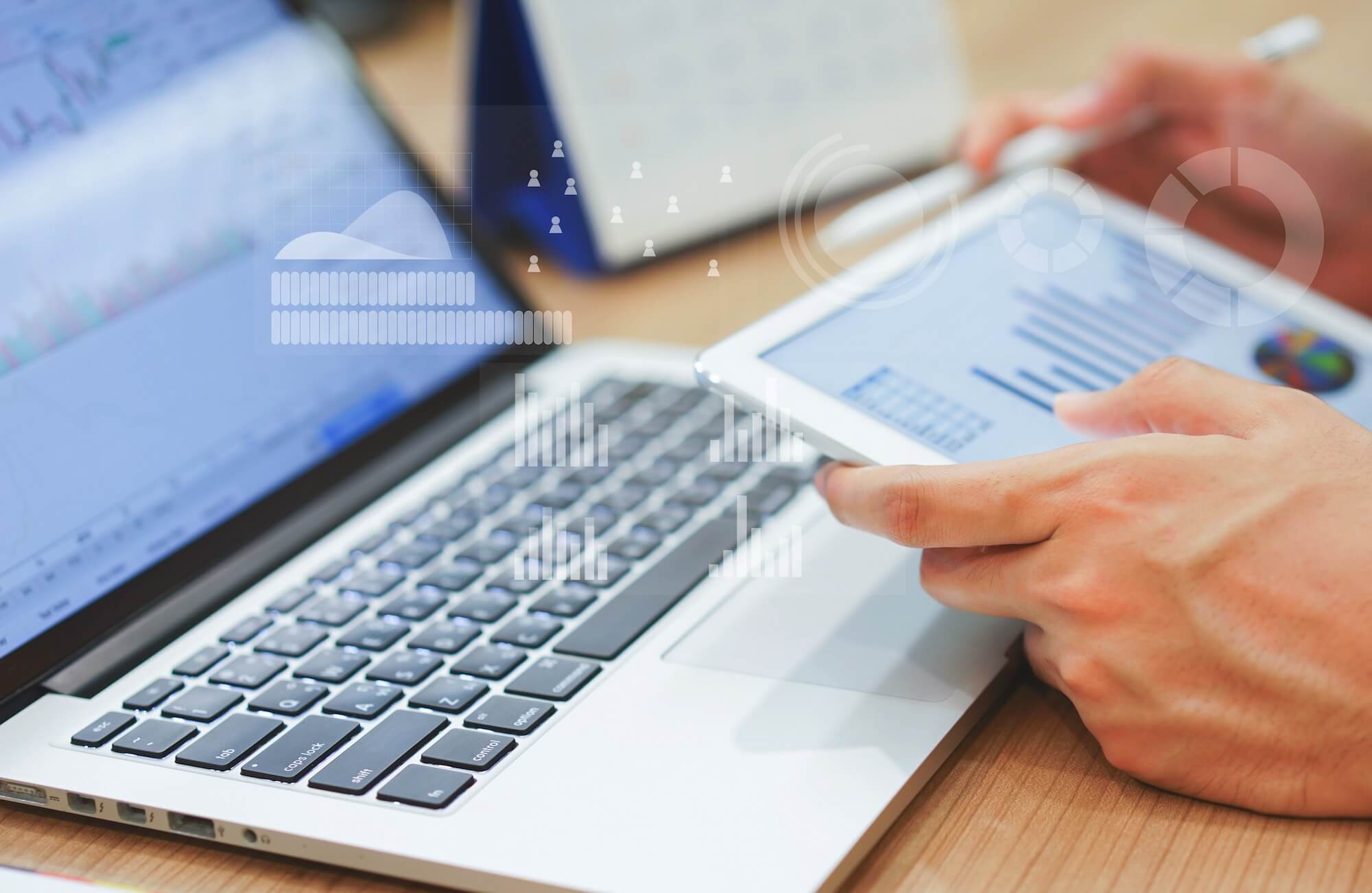 A person reviews a graph of data on a tablet while sitting in front of a laptop